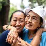 An older woman and her adult daughter hug each other and smile as they connect better through effective dementia communication skills.